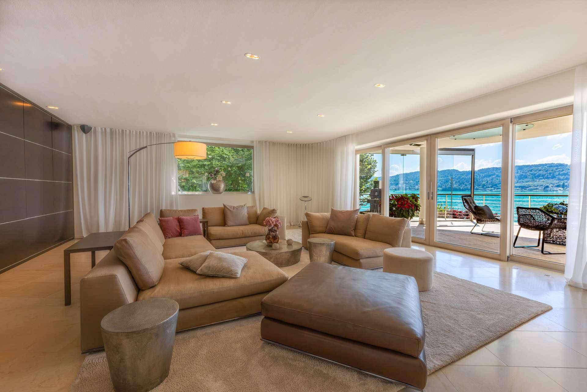 Helles Wohnzimmer mit bequemen Sofas, modernen Möbeln und großen Glasfronten mit Seeblick.