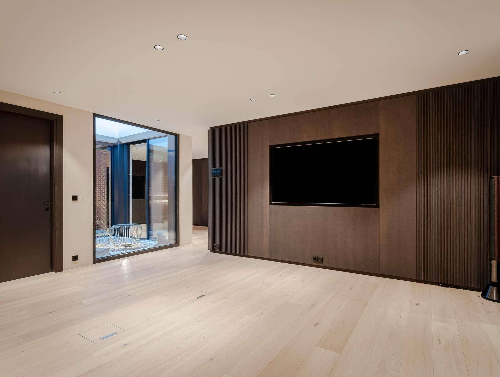 Leerer Raum mit Holzboden, dunkler Wandverkleidung und integriertem Fernseher.