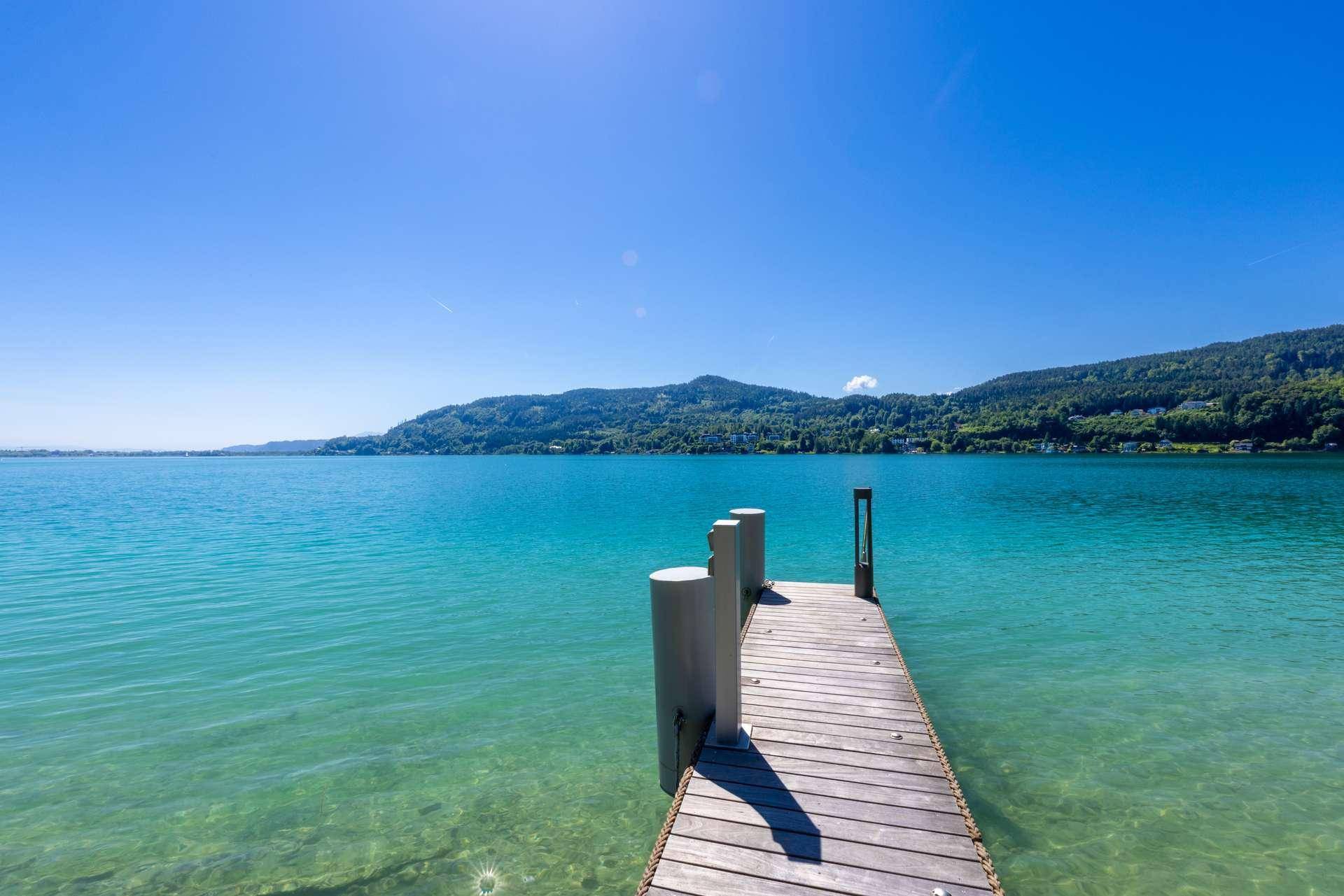 Kurzer Holzsteg ragt in das ruhige, klare Seewasser mit weitem Blick auf die umliegende Landschaft.