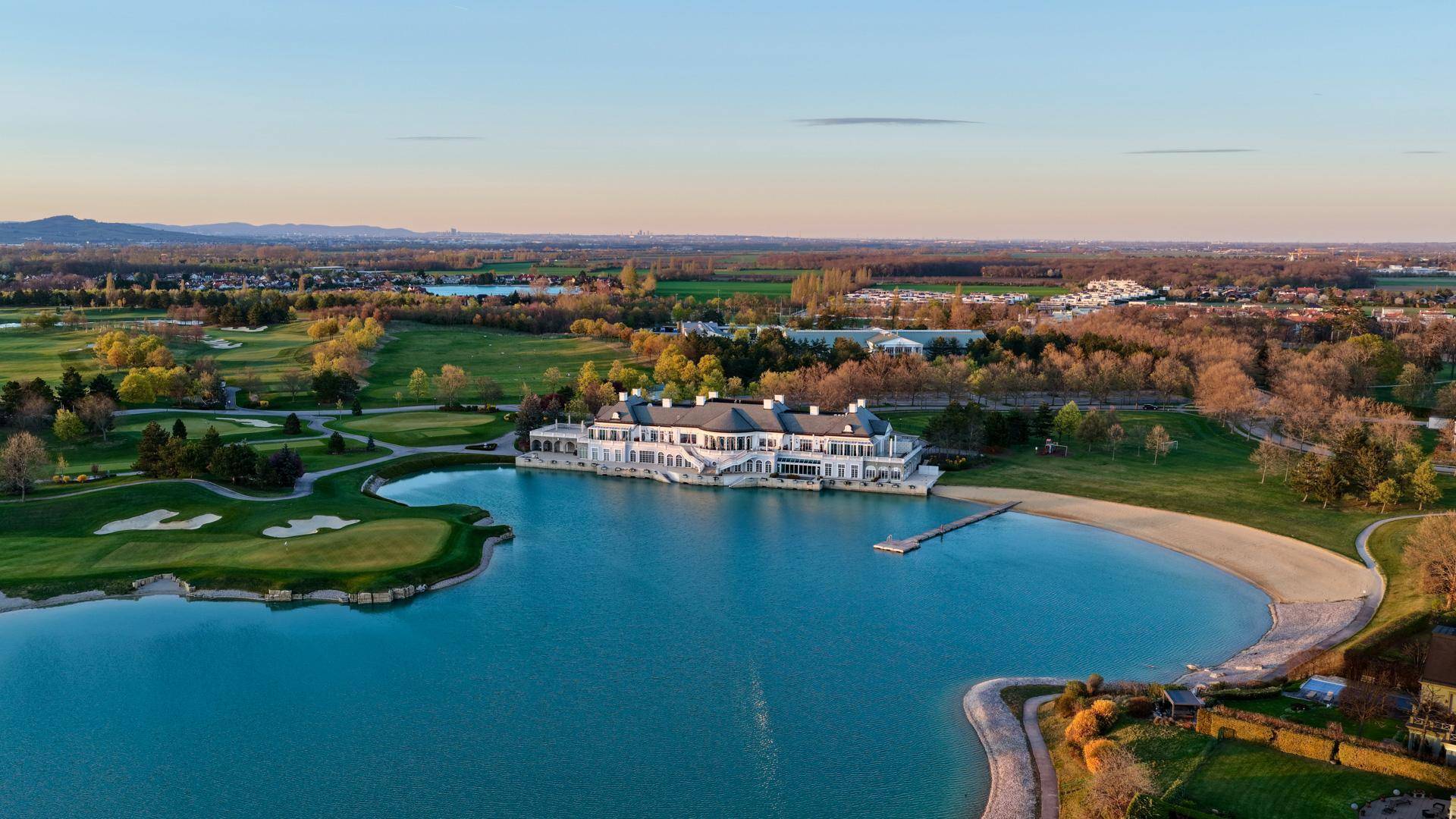 Panoramablick aus der Luft auf den türkisfarbenen See, den Golfplatz und die umliegende Landschaft.