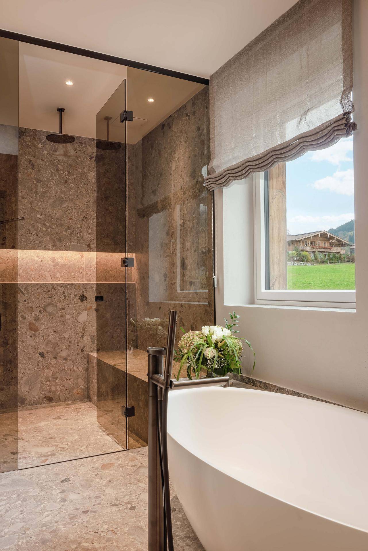 Elegantes Badezimmer mit freistehender Badewanne, großer Dusche und Blick ins Grüne.