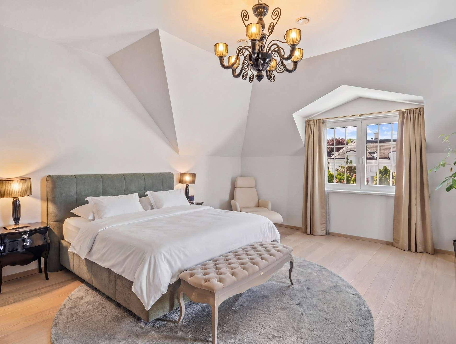 Helles Schlafzimmer im Dachgeschoss mit schrägen Wänden, Holzboden und elegantem Kronleuchter.