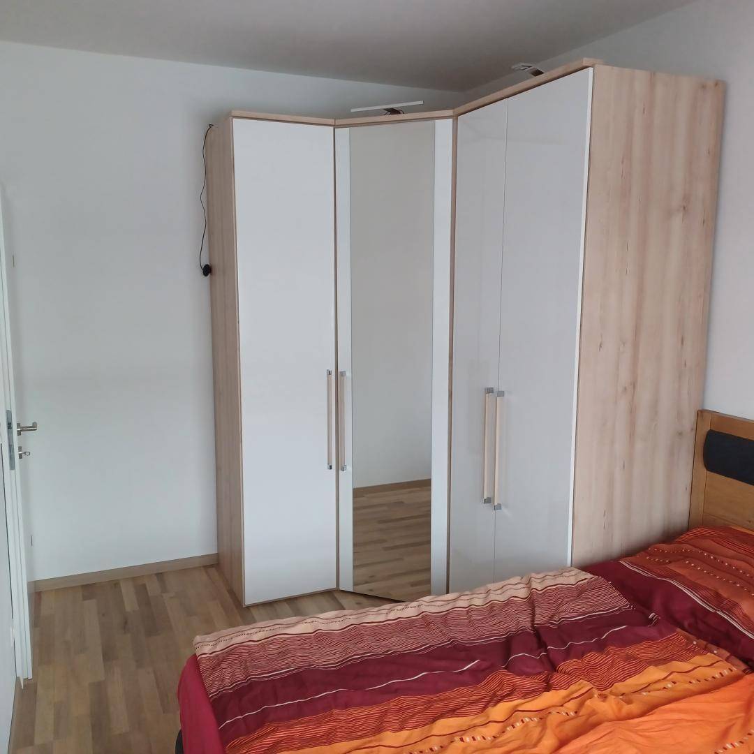 Schlafzimmer mit großem Eckkleiderschrank und einem Bett mit farbenfroher Bettwäsche.
