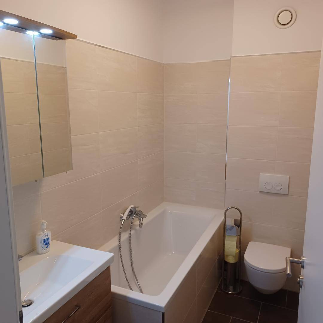Modernes Badezimmer mit Badewanne, wandhängendem WC und beigefarbenen Fliesen.
