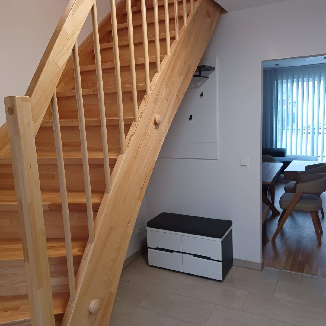 Heller Flur mit Holztreppe, die in die obere Etage führt, und hellem Fliesenboden.
