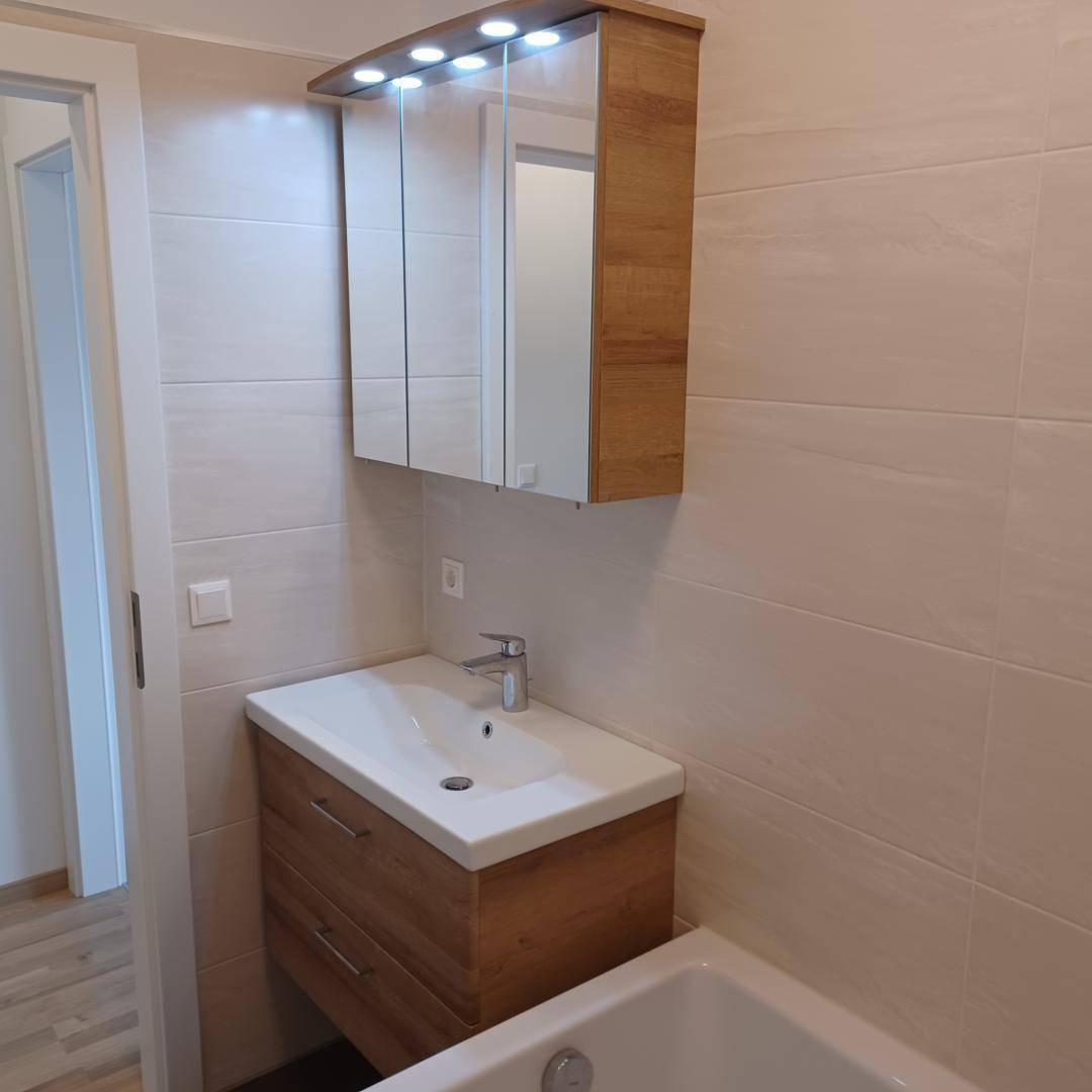 Badezimmer mit modernem Waschtischunterschrank, beleuchtetem Spiegelschrank und hellen Fliesen.