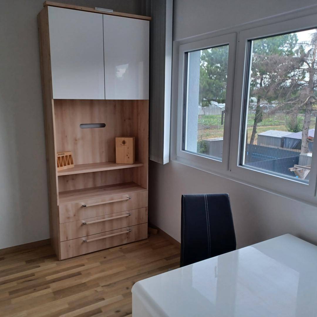 Heller Raum mit einem Schrank, einem Schreibtisch und einem Fenster mit Blick ins Grüne.