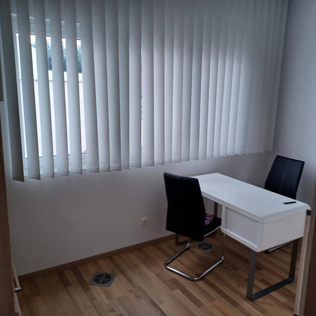 Arbeitszimmer mit Schreibtisch, zwei Stühlen und Fenster mit vertikalen Jalousien.
