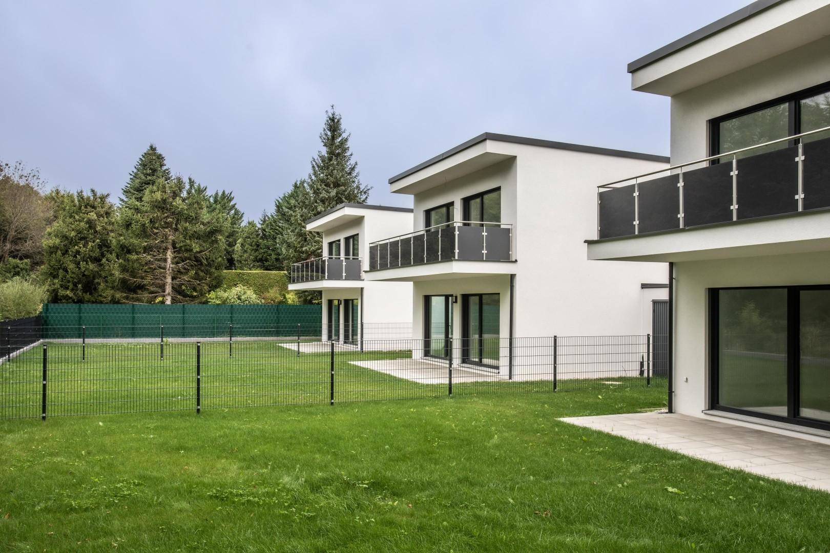 Drei moderne Reihenhäuser mit Balkonen, Gärten und weißer Putzfassade.