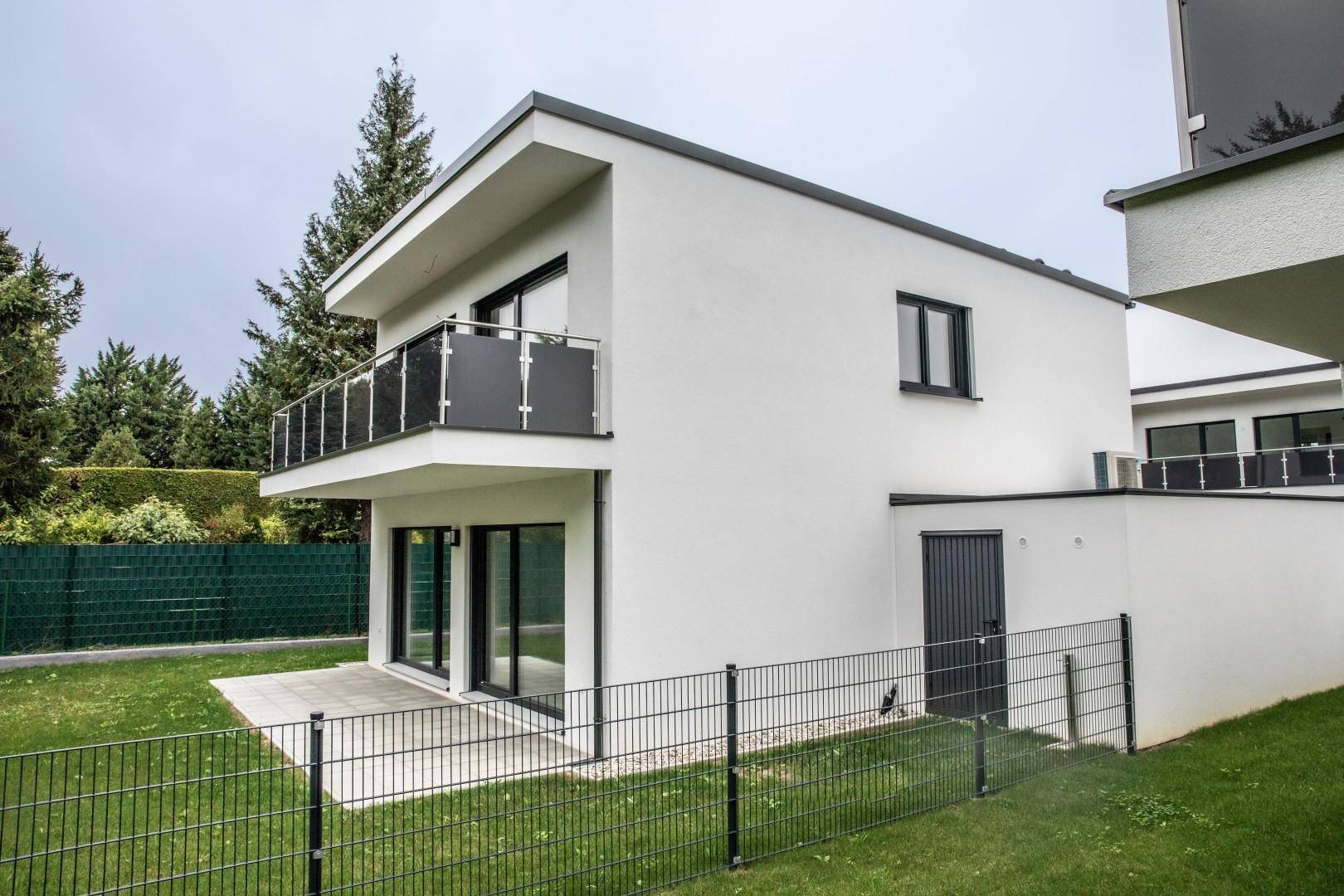 Seitenansicht eines modernen Hauses mit Balkon, Garten und schlichtem Design.