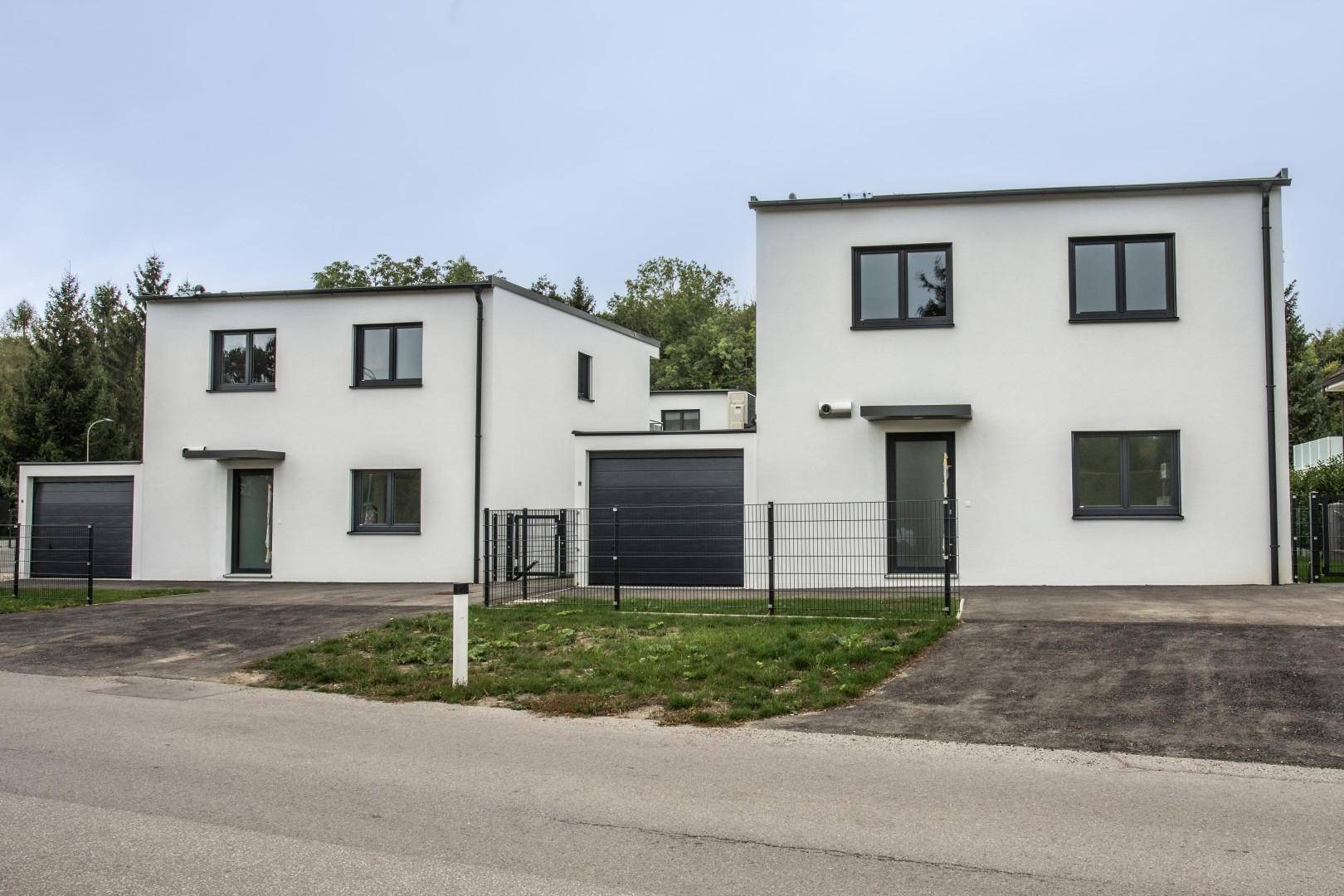 Moderne Reihenhäuser mit Garagen und weißer Fassade entlang einer ruhigen Straße.