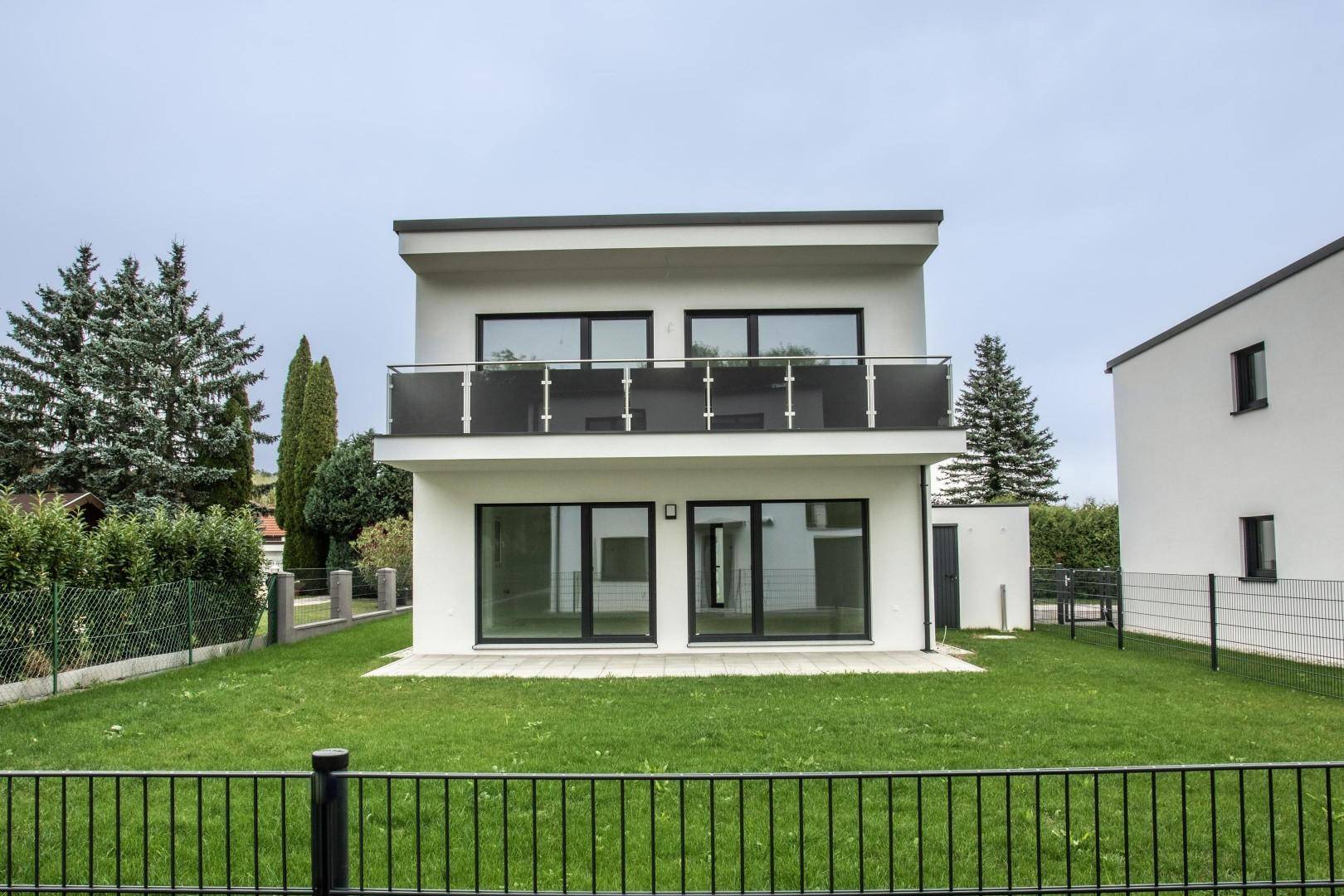 Vorderansicht eines modernen Einfamilienhauses mit Balkon und grünem Vorgarten.