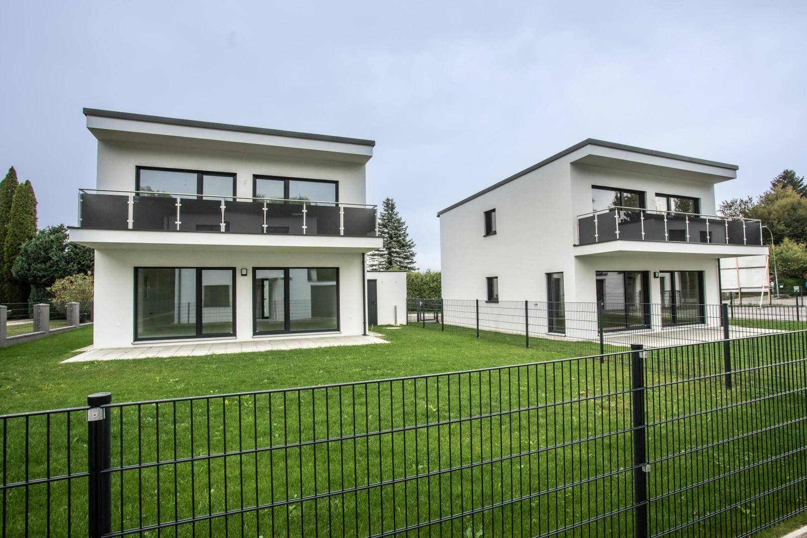 Zwei moderne Häuser mit weißen Fassaden, Balkonen und umzäunten Gärten.