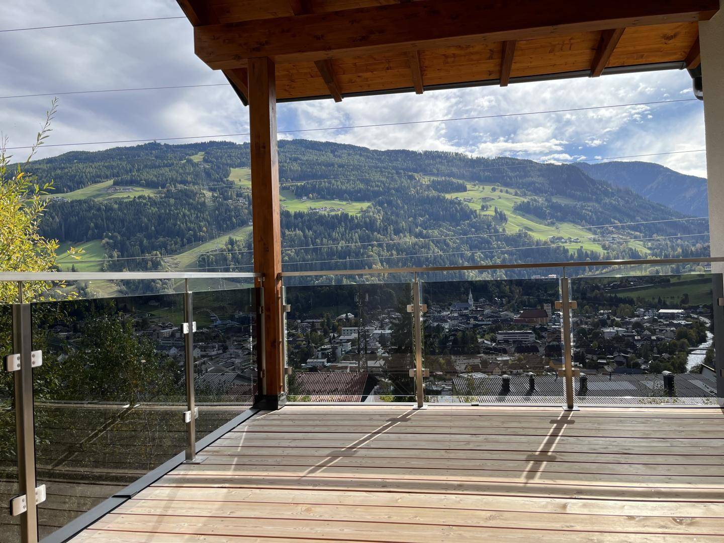 Großer Holzbalkon mit Glasgeländer und beeindruckendem Panoramablick auf das Tal und die Berge.