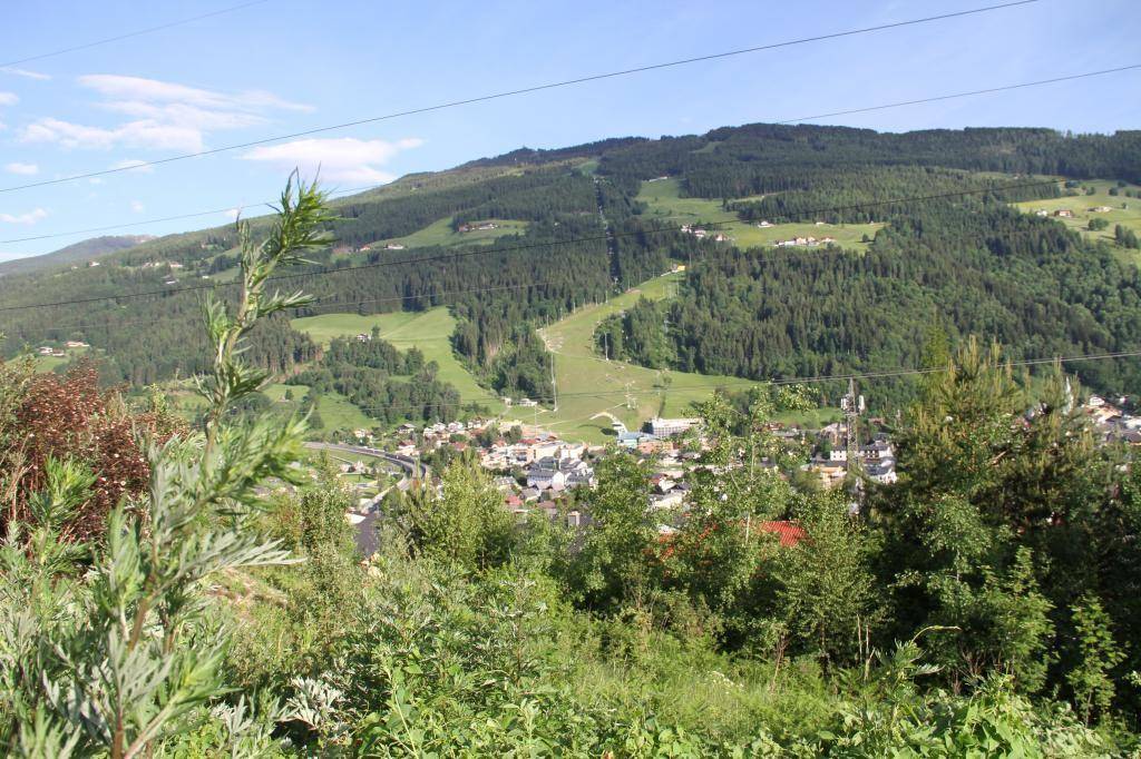 Weitläufiger Blick auf eine Berglandschaft mit einem Tal und einer kleinen Ortschaft.