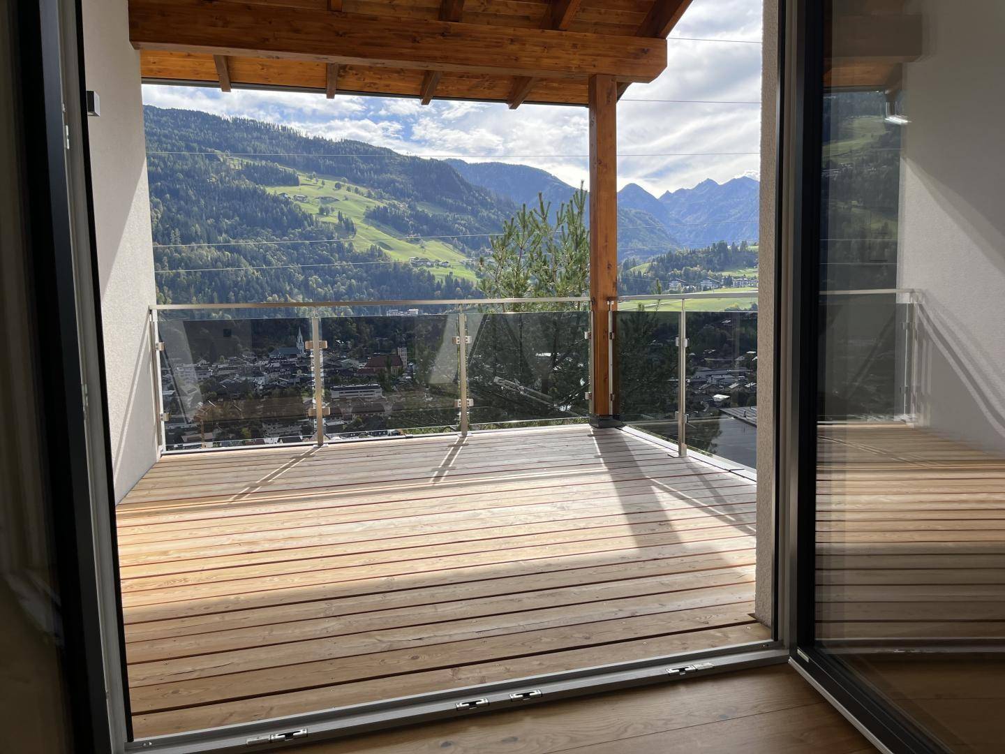 Blick von innen auf einen modernen Holzbalkon mit Glasgeländer und beeindruckendem Bergpanorama.