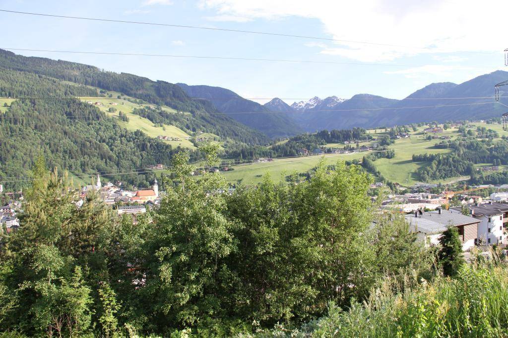 Weitläufiger Panoramablick über ein grünes Tal mit Bergen und einer malerischen Stadt im Hintergrund.