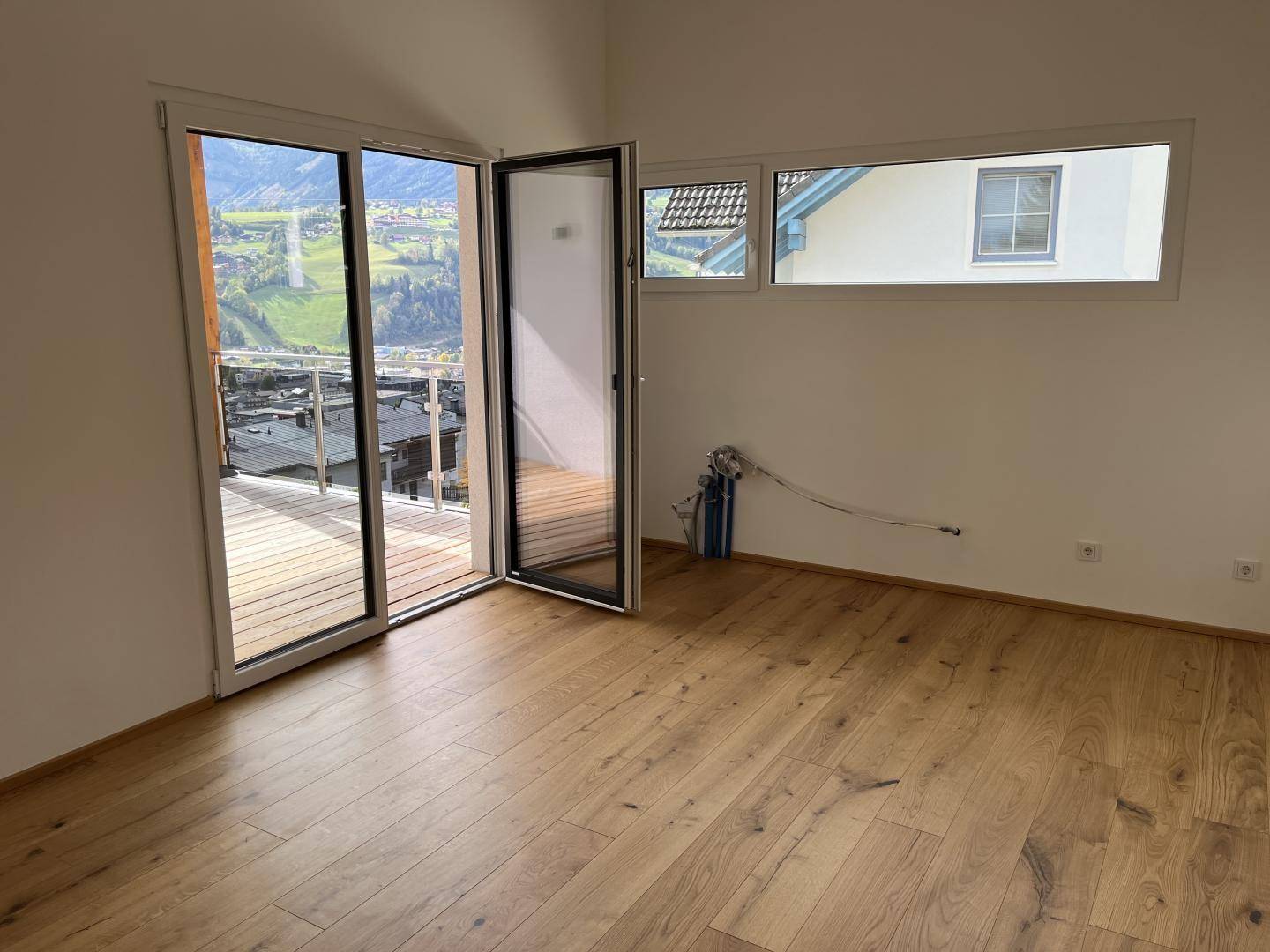 Heller Raum mit Holzboden, großen Schiebetüren zum Balkon und weitem Blick auf die Berglandschaft.
