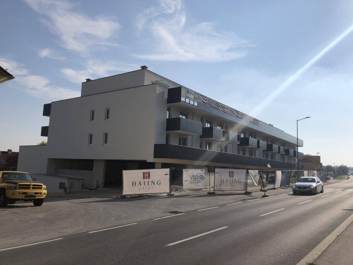 Modernes Wohngebäude im Bauzustand mit dunklen Balkonen und Baustellenabsperrungen an der Straße.
