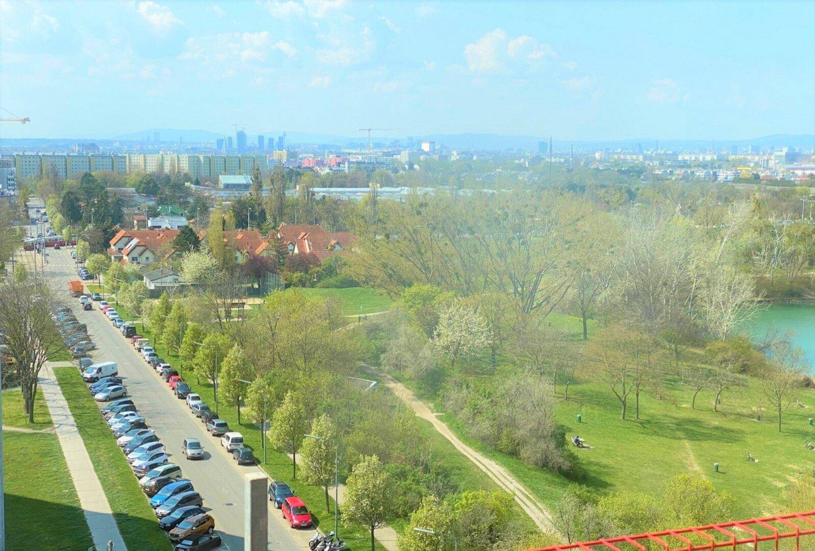 Weitläufiger Blick über die Stadt, grüne Parkanlagen und einen Fluss von einer oberen Etage.