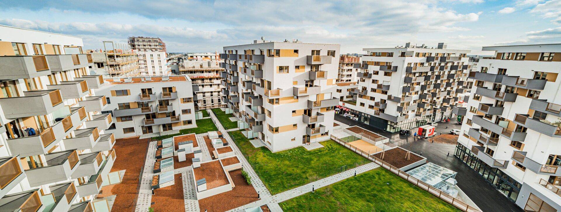 Vogelperspektive auf eine moderne Wohnanlage mit mehreren Gebäuden, grünen Innenhöfen und Wegen.