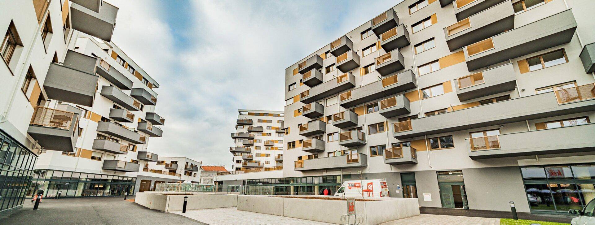 Moderne Wohngebäude mit zahlreichen Balkonen und einer gepflasterten Zufahrt unter bewölktem Himmel.