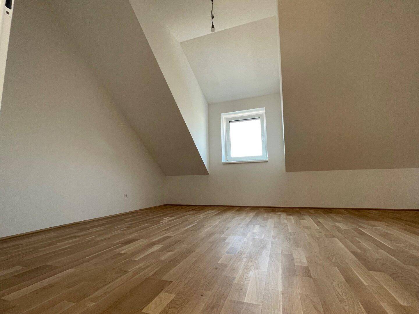 Helles Zimmer mit Holzboden und Dachschrägen, ideal als Schlaf- oder Arbeitsbereich.