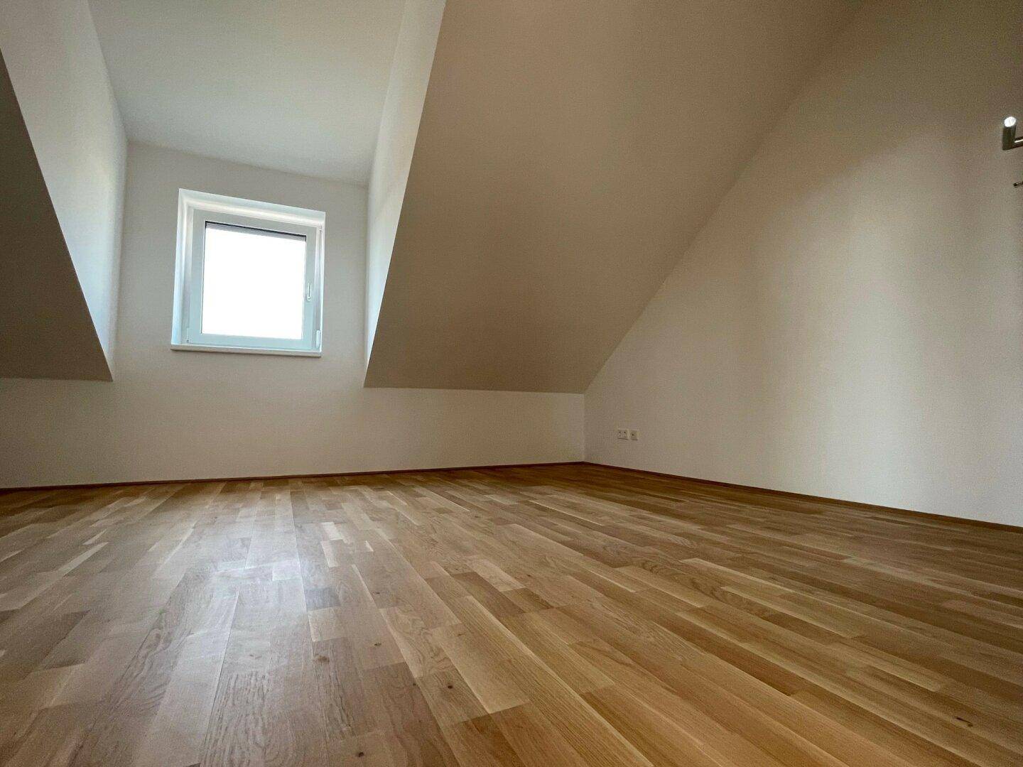 Geräumiges Zimmer mit Holzboden und markanten Dachschrägen, ideal für ein Schlafzimmer.