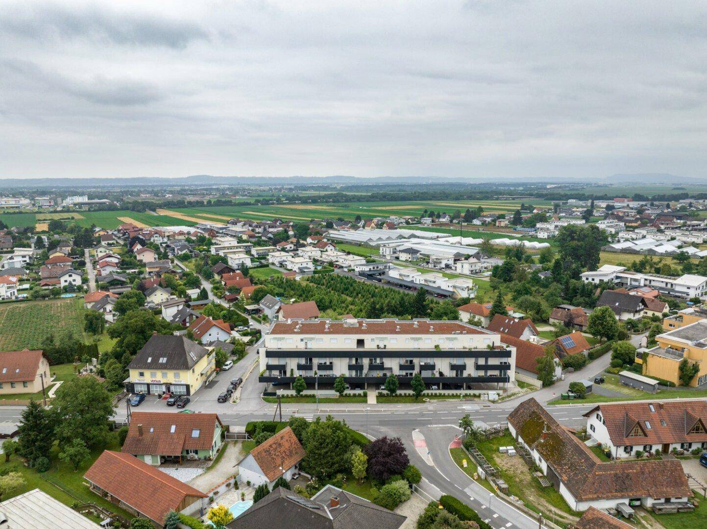 Weitläufige Luftaufnahme eines Wohnkomplexes in ländlicher Umgebung mit Feldern, Wiesen und Häusern.