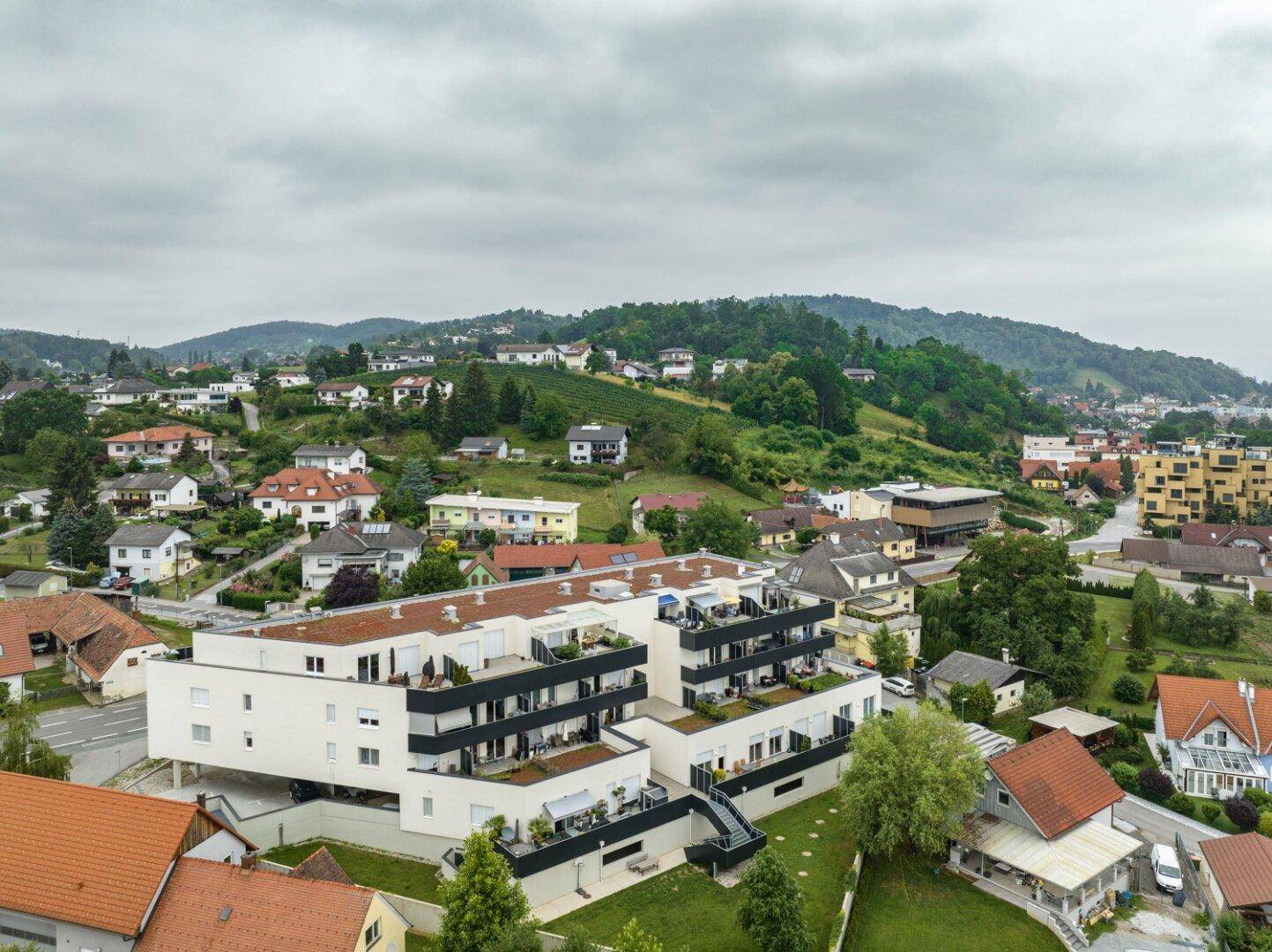 Luftaufnahme eines modernen Wohnkomplexes mit Terrassen und Balkonen in einer grünen Umgebung.