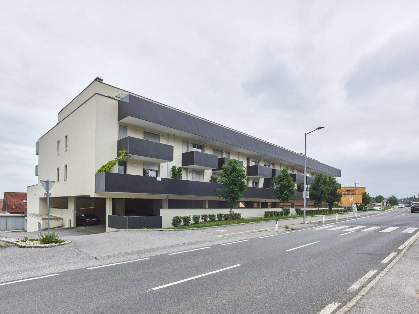 Modernes Wohngebäude mit dunklen Balkonen und integrierter Tiefgarage an einer ruhigen Straße.