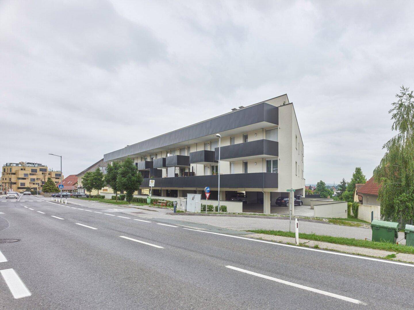 Modernes Wohngebäude mit dunklen Balkonen und integrierter Tiefgarage an einer Hauptstraße.