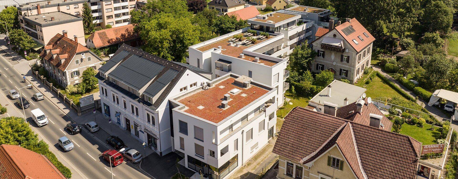 Luftaufnahme eines Wohnkomplexes mit Flachdächern, Solaranlagen und umliegender Bebauung.