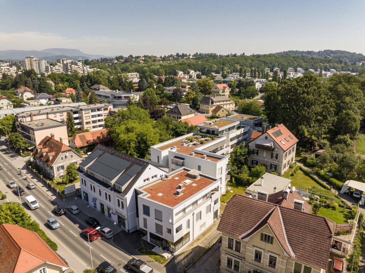 Weitläufige Luftaufnahme eines Wohngebiets mit modernen Gebäuden, viel Grün und Stadtblick im Hintergrund.