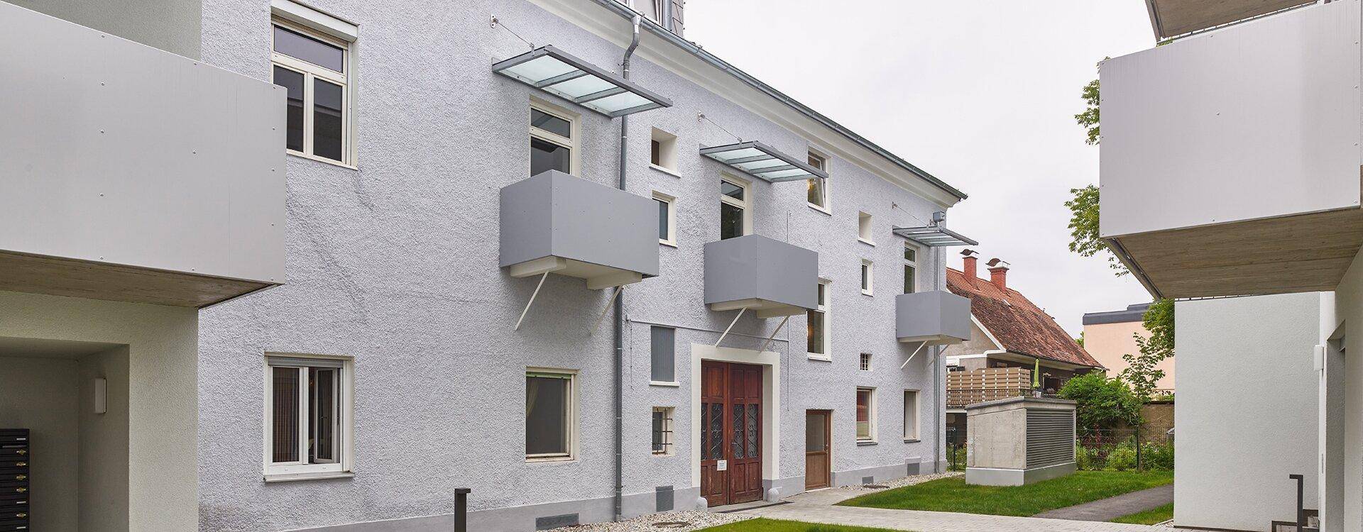 Seitenansicht eines Gebäudes mit kleinen, modernen Balkonen und einem gepflegten Eingangsbereich.