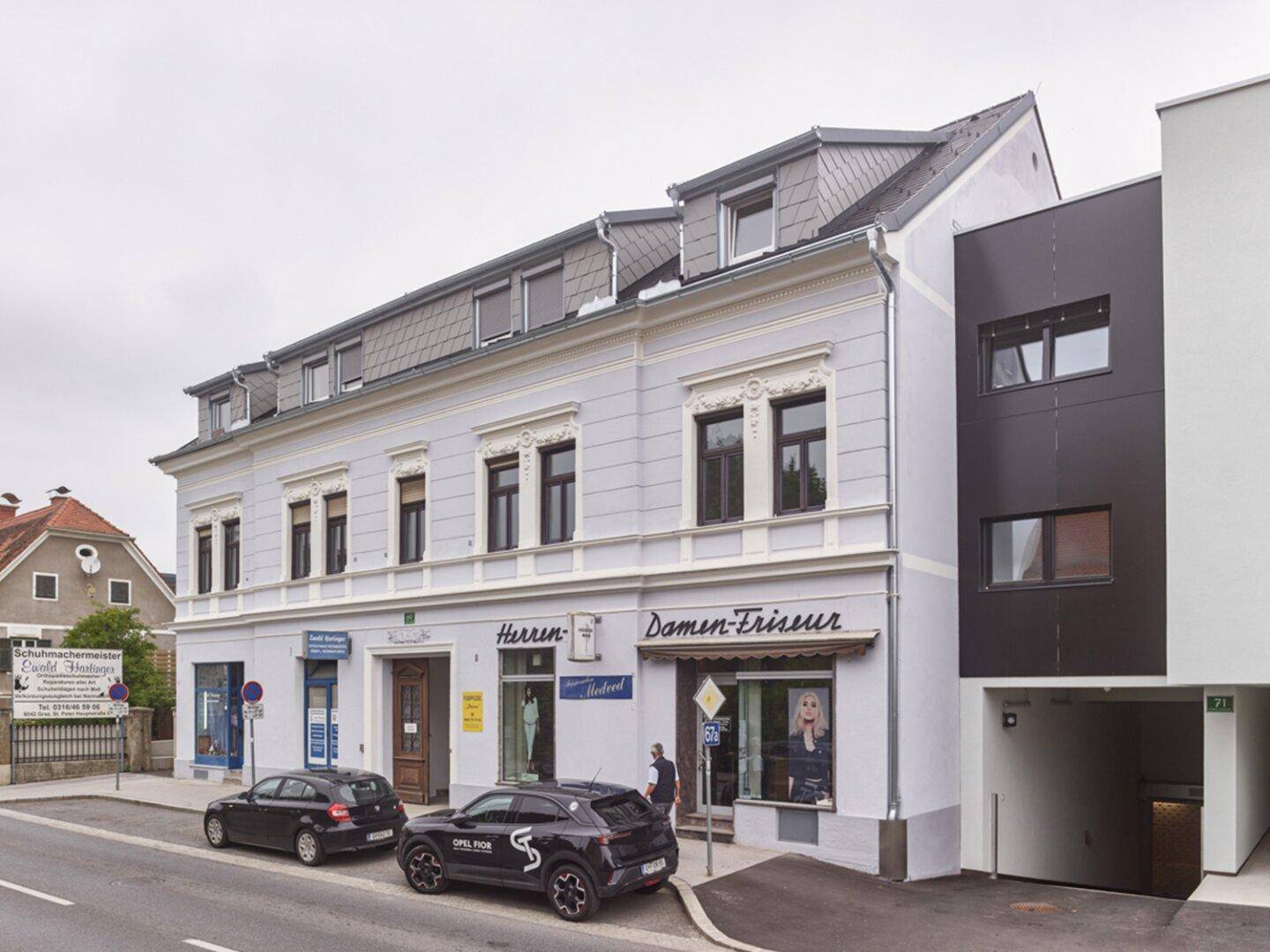 Fassade eines renovierten Altbaus mit angrenzendem modernen Neubau und Geschäften im Erdgeschoss.
