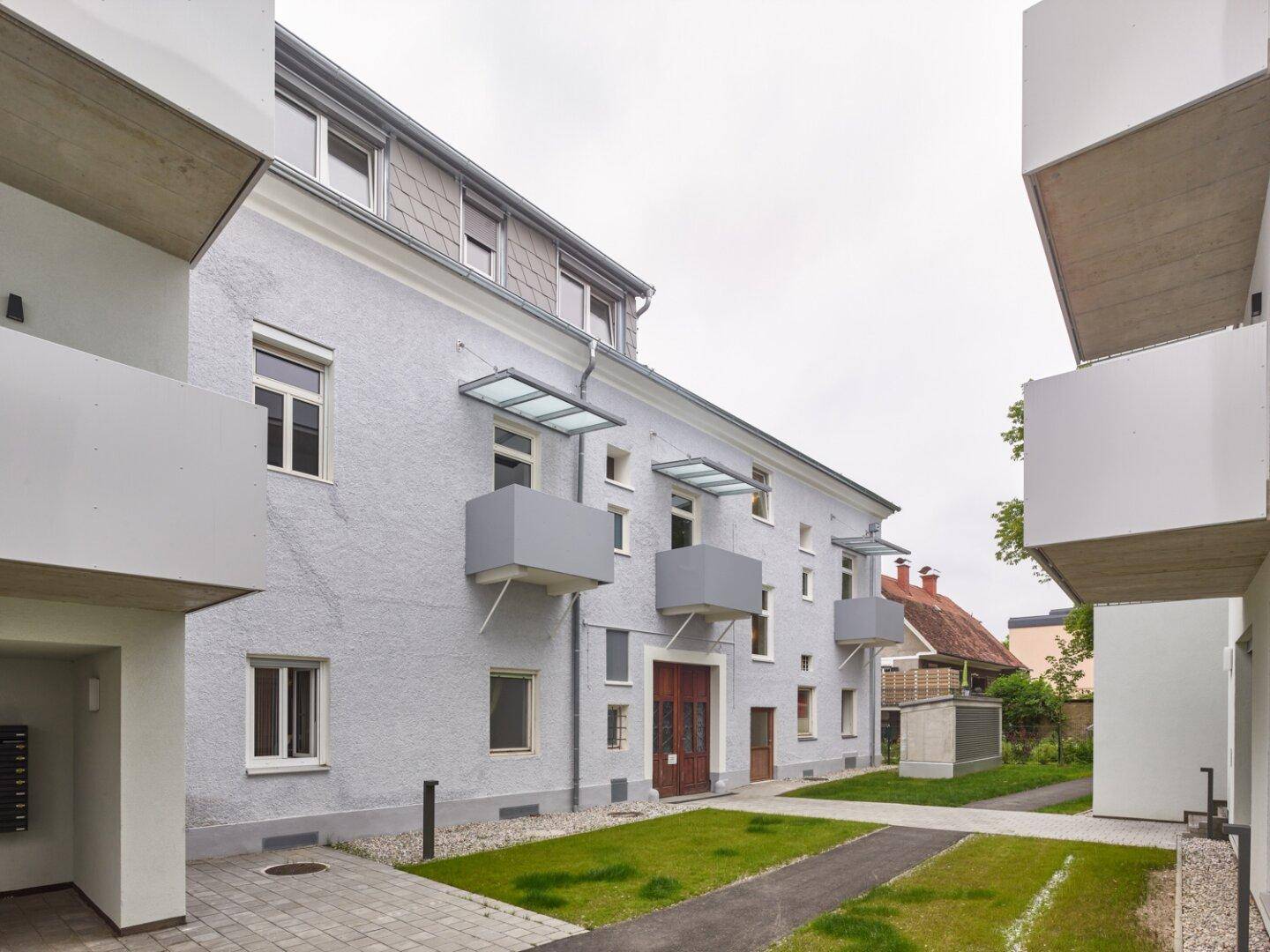 Seitenansicht eines Wohngebäudes mit kleinen Balkonen und einem gepflegten Außenbereich.