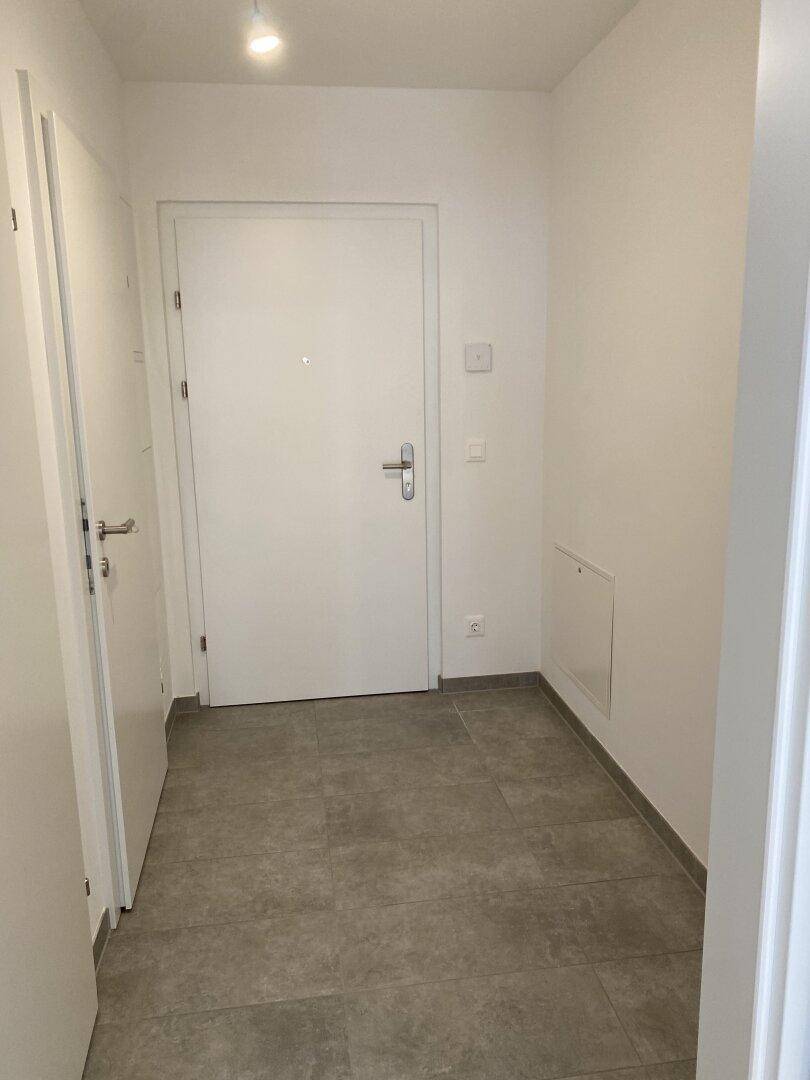 Heller Eingangsbereich mit modernen grauen Fliesen und weiß gestrichenen Wänden.