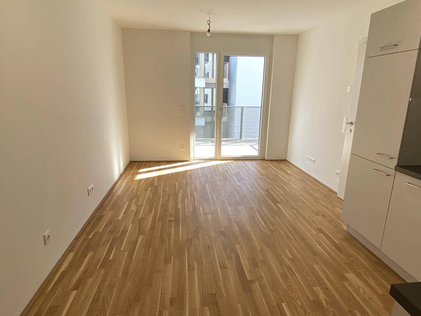 Lichtdurchfluteter Wohnbereich mit Parkettboden und Zugang zu einem Balkon.