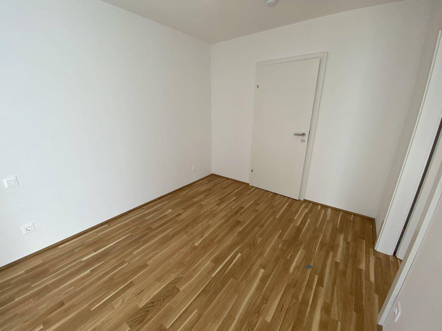 Geräumiges Schlafzimmer mit hellem Parkettboden und weiß gestrichenen Wänden, bereit zur Einrichtung.