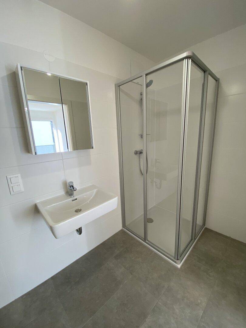 Modernes Badezimmer mit Duschkabine, Waschbecken und Spiegelschrank in hellen Farben.