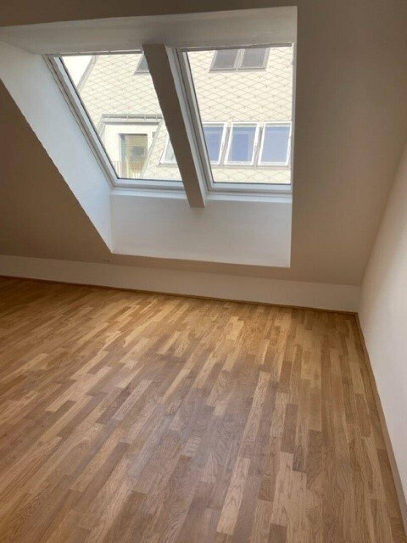 Helles Zimmer im Dachgeschoss mit Holzparkett und großen Dachfenstern.