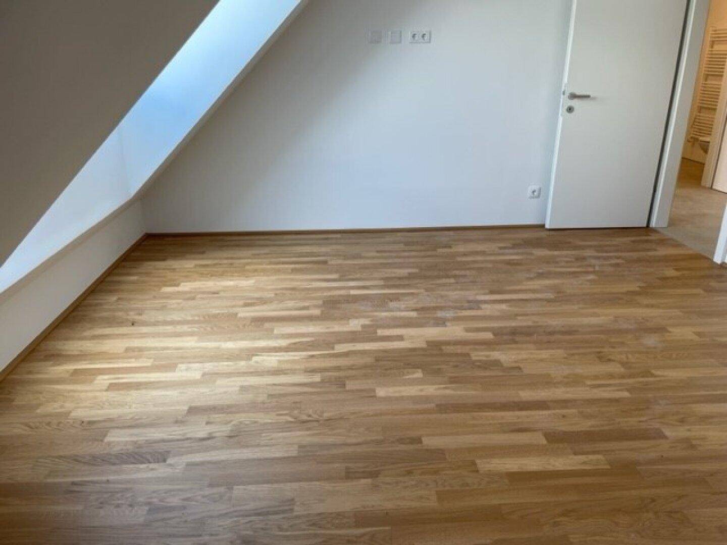Dachgeschosszimmer mit Holzparkett und weiß gestrichenen Wänden, bereit zum Einrichten.