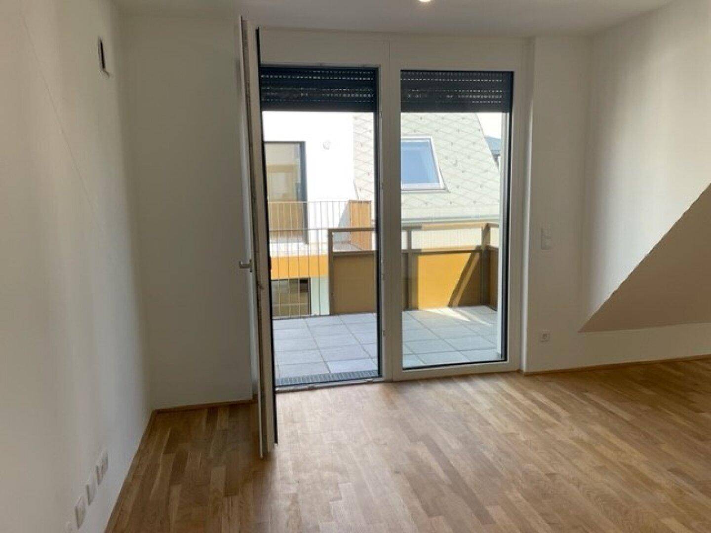 Heller Raum mit Balkonzugang und Holzparkett, ideal für Wohn- oder Schlafbereich.