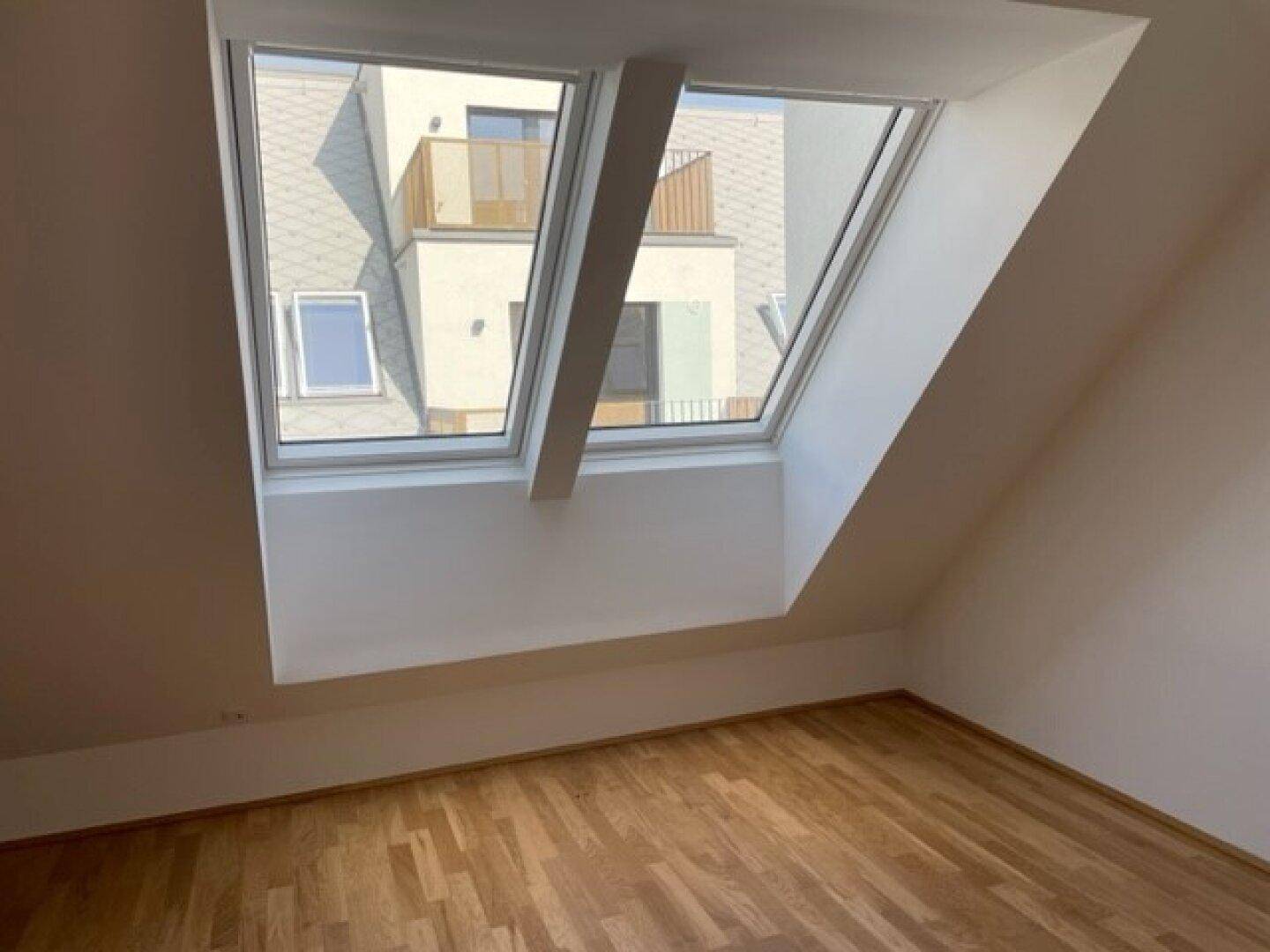 Helles Dachgeschosszimmer mit zwei großen Dachfenstern und Holzparkettboden.