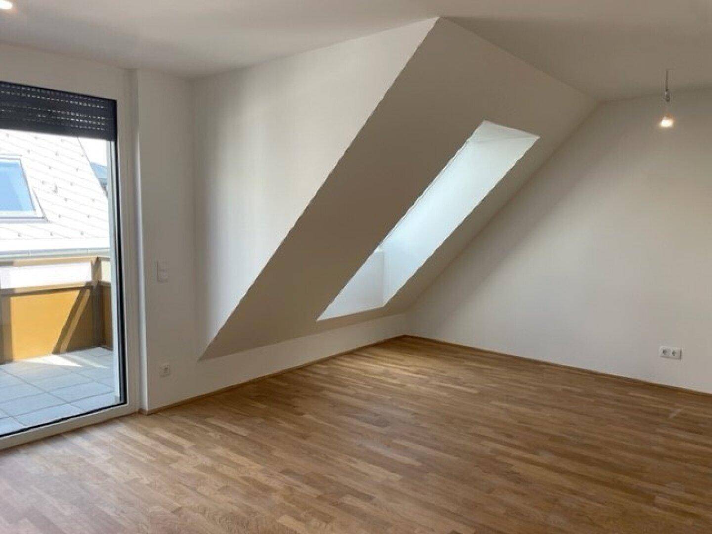 Geräumiger Wohnbereich mit Balkonzugang, Holzparkett und schrägen Wänden.