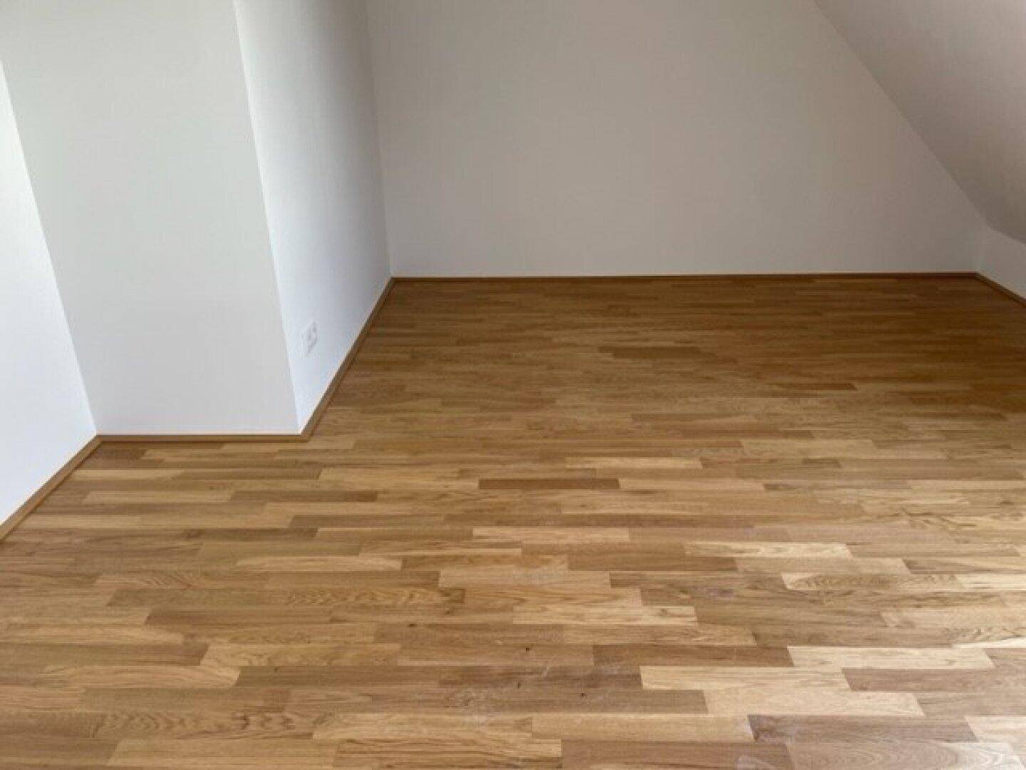 Geräumiges Zimmer mit hellem Holzparkett und schrägen Wänden im Dachgeschoss.