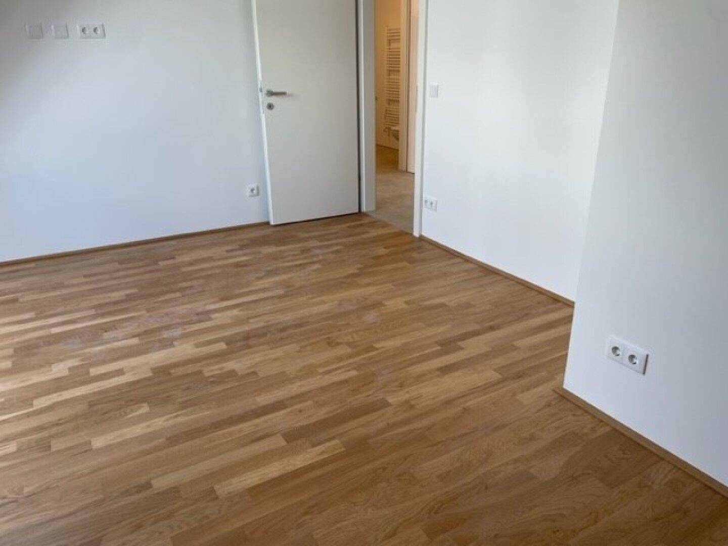 Leeres Zimmer mit Holzparkett und Zugang zu einem weiteren Bereich.