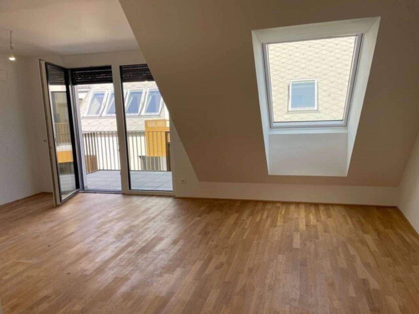 Lichtdurchfluteter Wohnraum mit Balkonzugang, Dachfenster und Holzparkett.