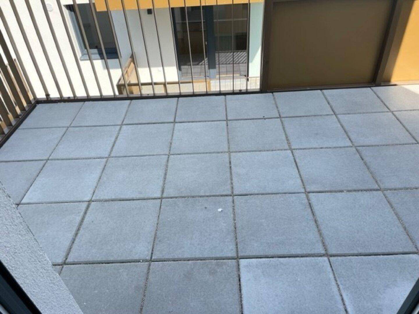Balkon mit grauen Fliesen und Metallgeländer, bietet einen Blick auf die Umgebung.